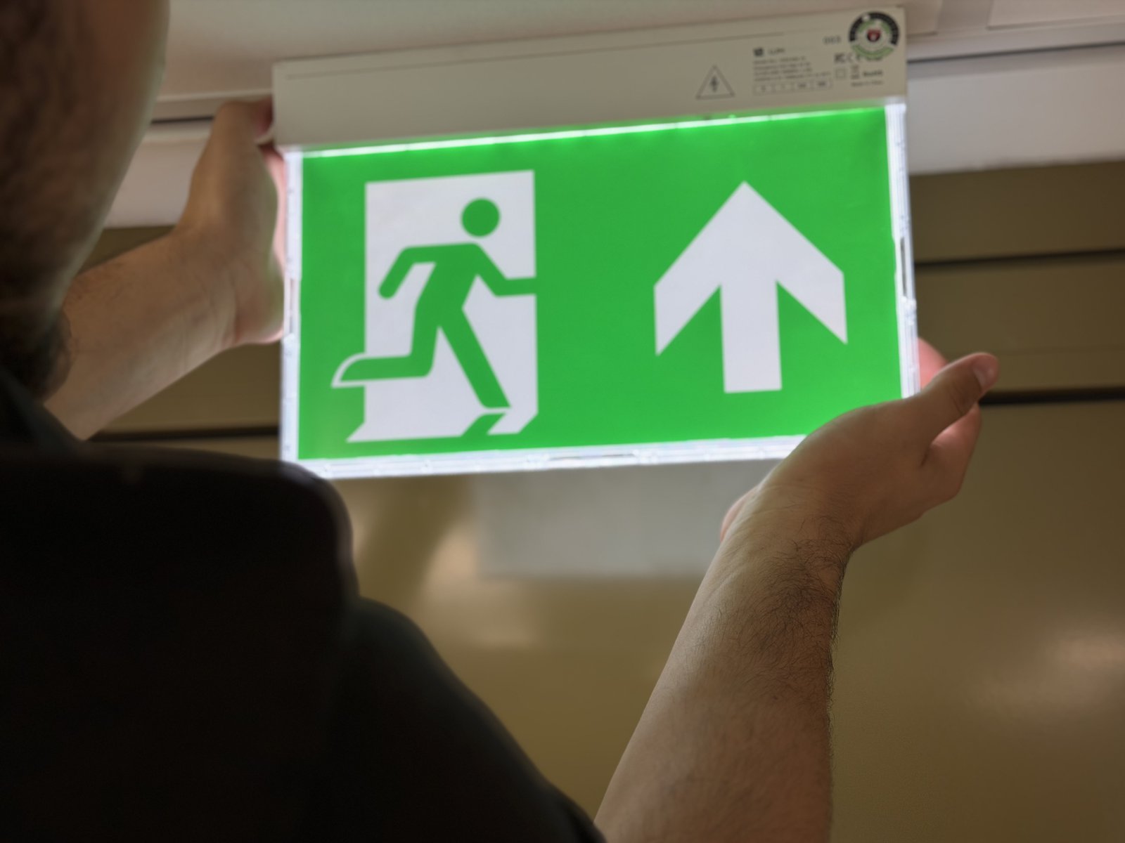 Monteur installeert een groen vluchtroutebordje (noodverlichting)